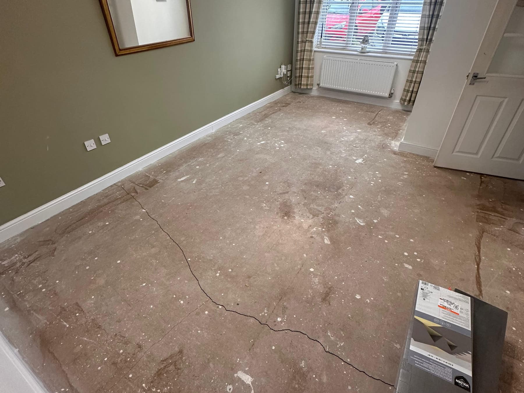 A bare room with cracked, patchy screed where the old floor covering has been lifted
