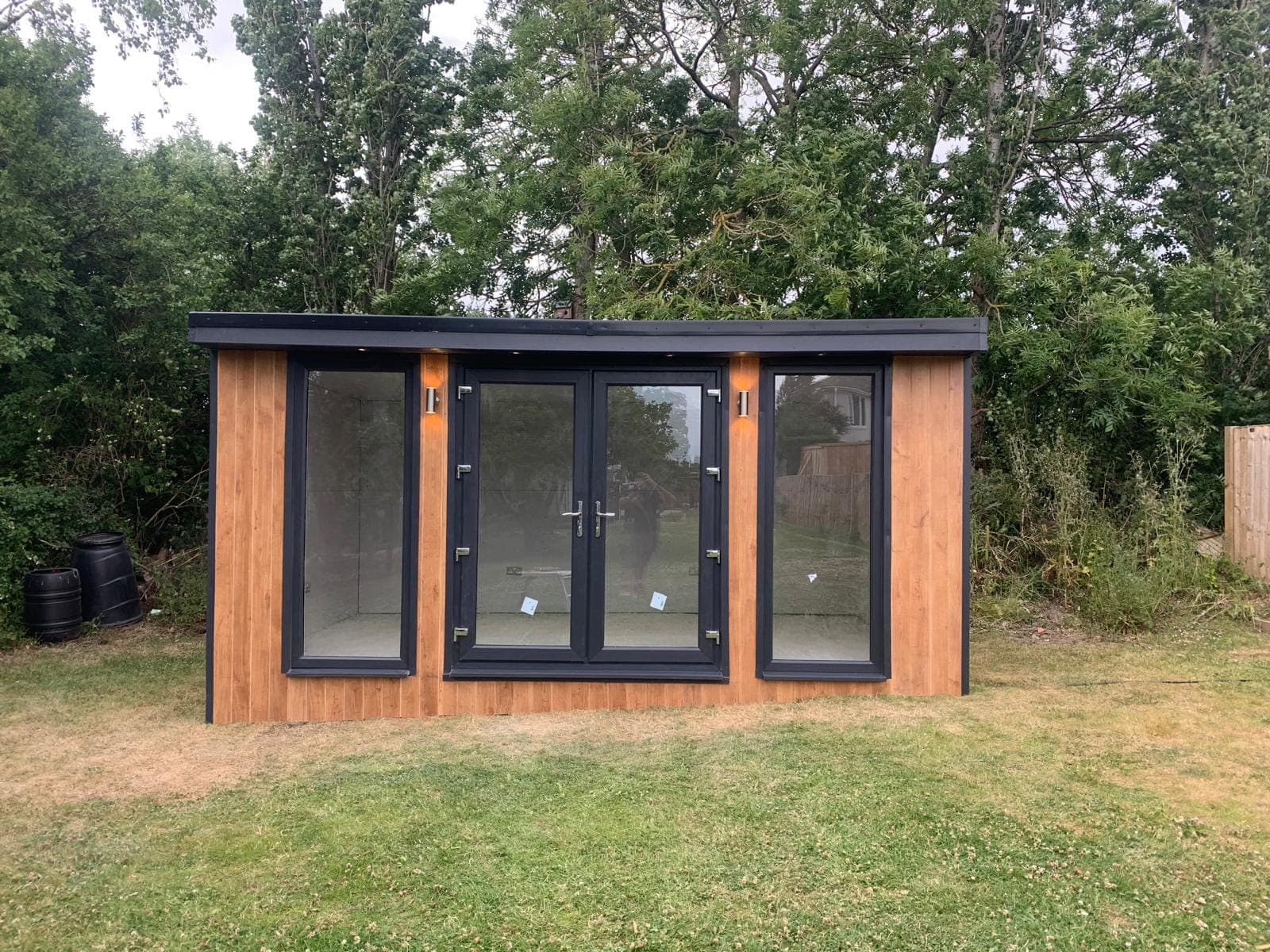 The same garden room finished in cedar cladding with French doors and full-height windows either side