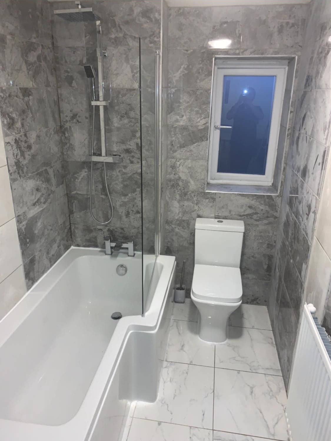 A finished bathroom with grey marble-effect tiling and a shower bath
