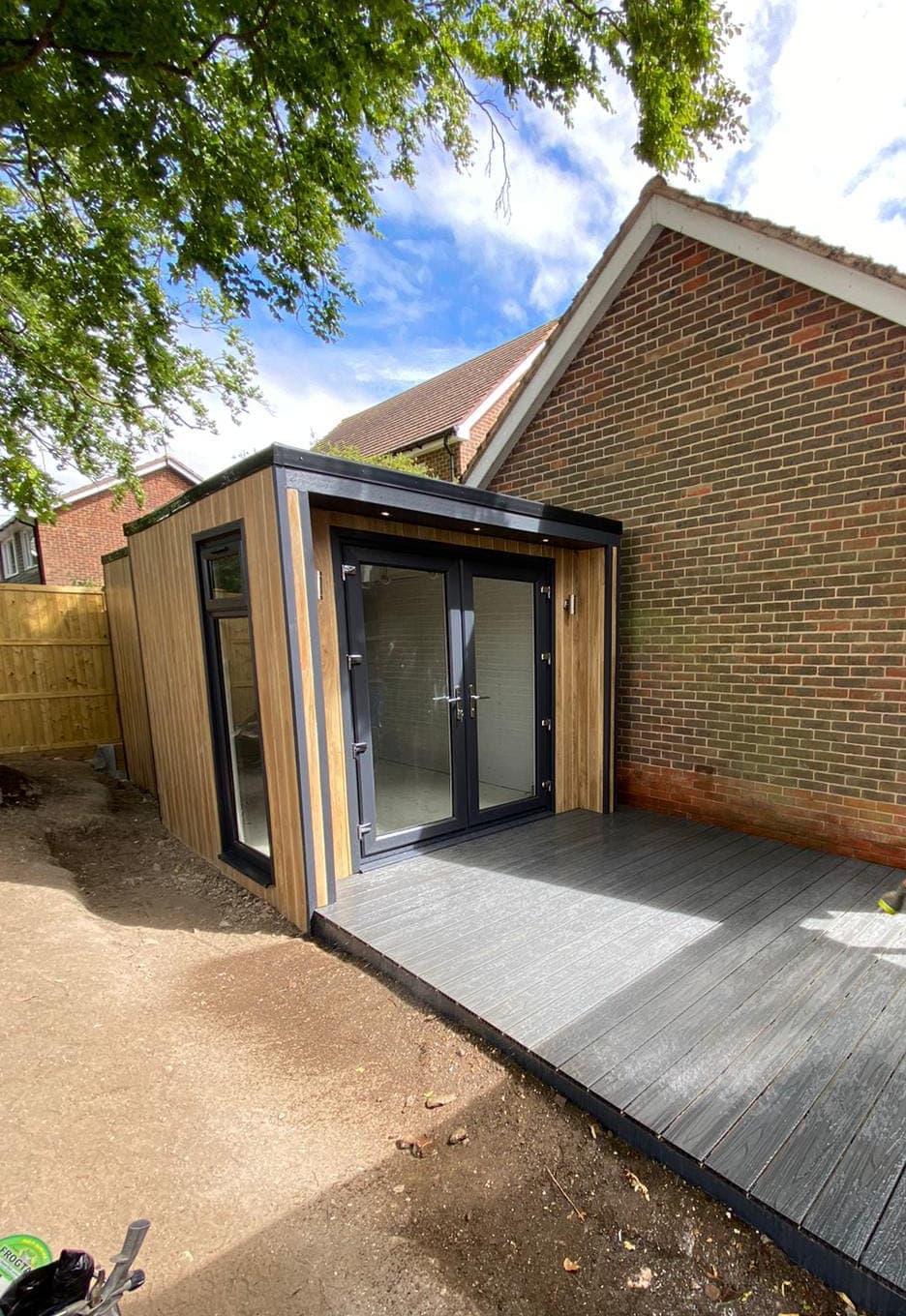 Grey composite decking laid up to the doors of a cedar-clad garden room