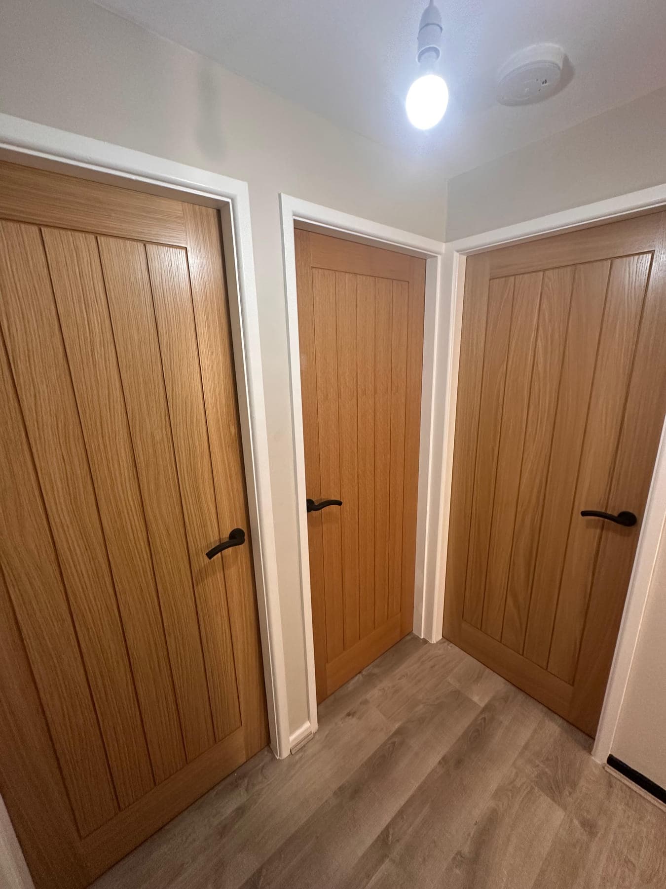Three oak cottage doors hung off a landing, with white architrave and wood-effect flooring