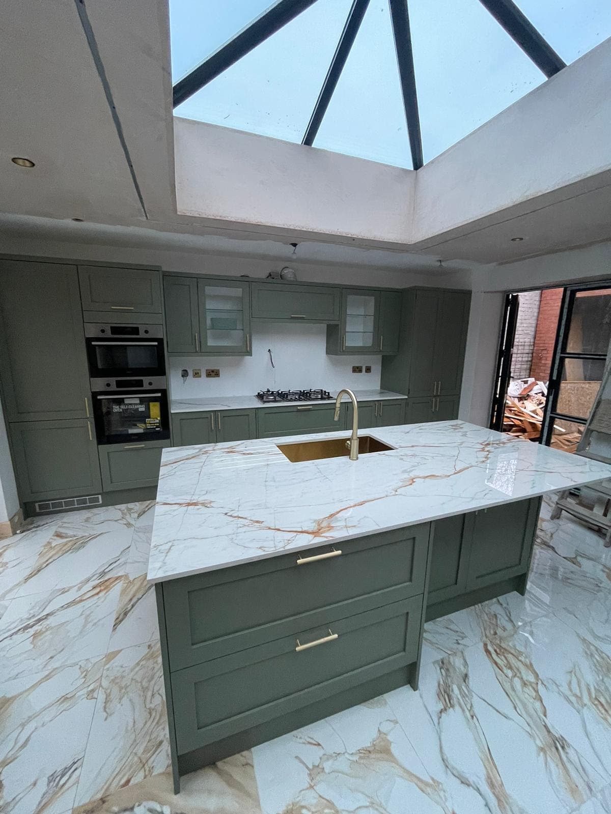 A sage green shaker kitchen with a marble-topped island beneath a glazed lantern roof